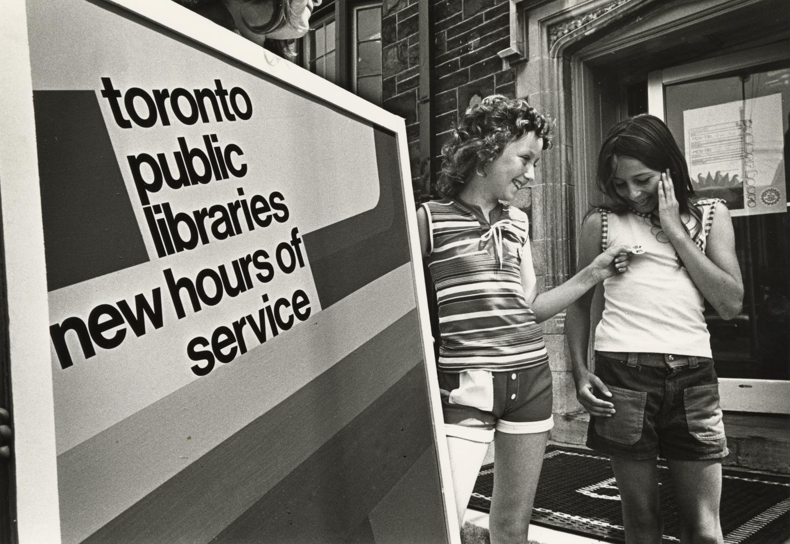 Two girls standing beside library sign. 