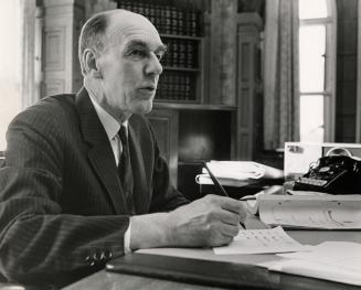 Robert Stanfield sitting at his desk with pen in hand in his parliamentary office.