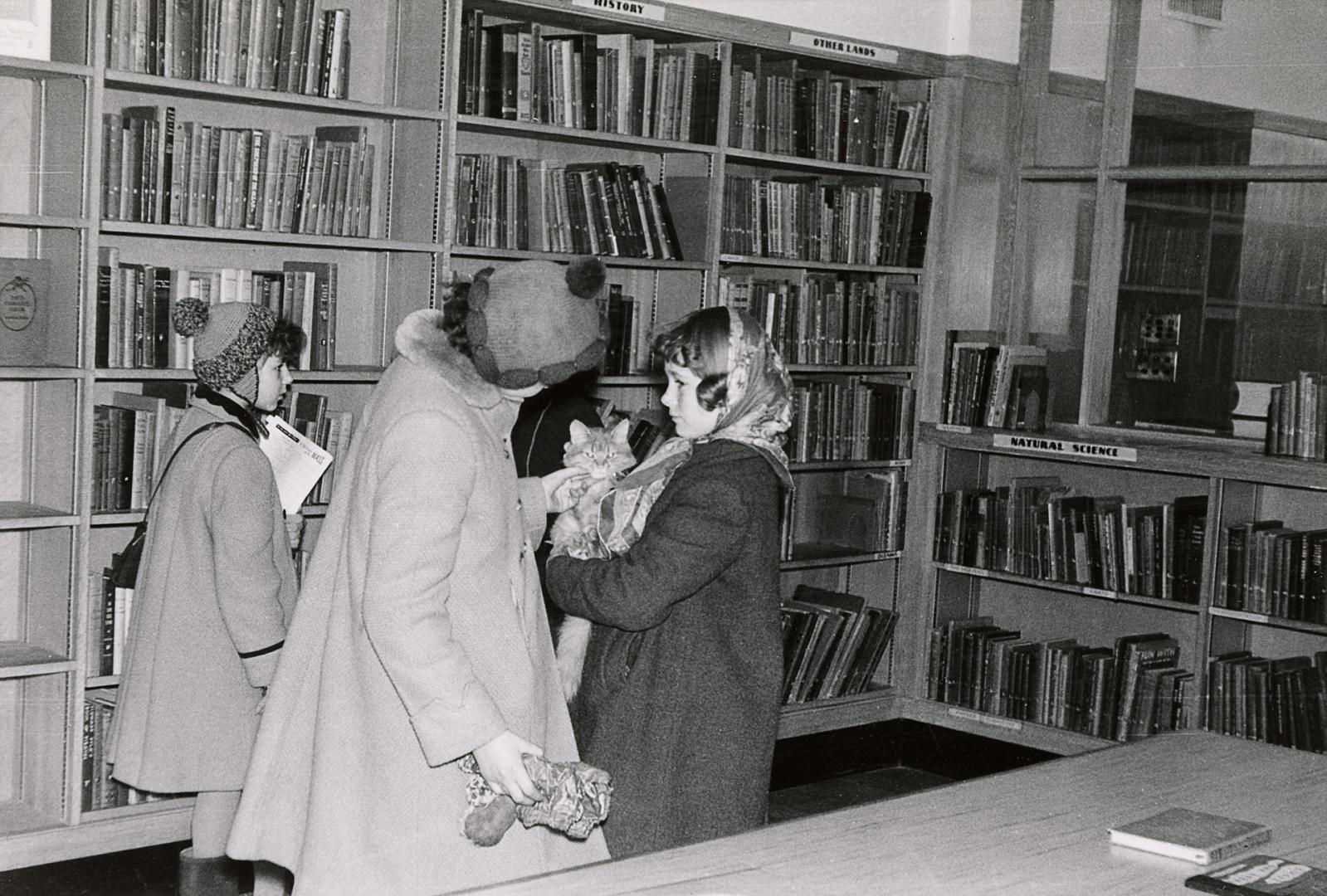 Picture of interior of library with 3 children. One child is holding a cat. 