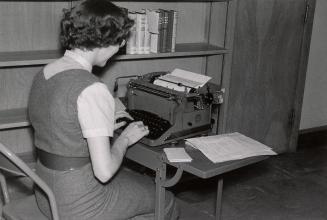 A woman sitting a desk typing on a typewriter.