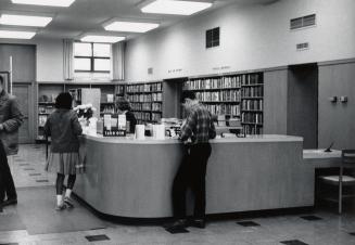 Picture of interior of library with staff at enquiry desk. 