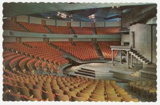 Color photograph of a stage surrounded by theatre chairs.