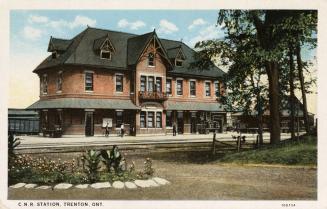 Colorized photograph of a two story railway station with gabled roofs.