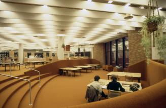 Picture of a sunken reading room in a library with orange carpeting and large tables. 