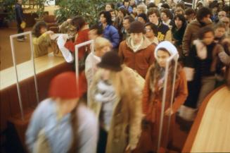 Picture of a crowd of people moving through an exit gate with blurred figures in the foreground…