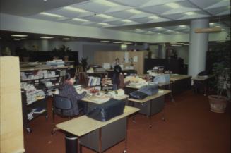 Picture of an office area in a library with several people at desks and shelving all around. 
