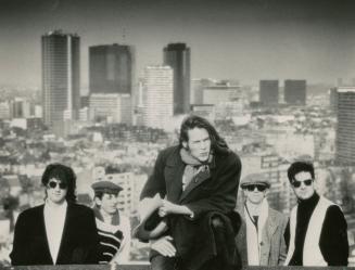 Four young men in foreground ascending a hill. Background is a cityscape.