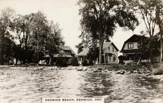 Black and white photograph of three cottages on the shore of a body of water,