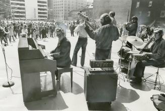 From behind six musicians playing piano. electric guitar, trumpet, drums and clarinet in a conc…