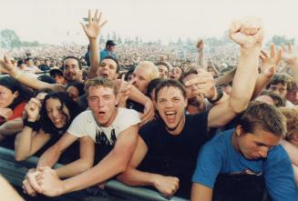 Crowd of young men in audience during day time. Some with fists up. 