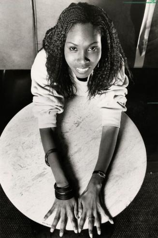 Young woman smiling in sweater with stacked bracelets spreads her hands over a small table. 