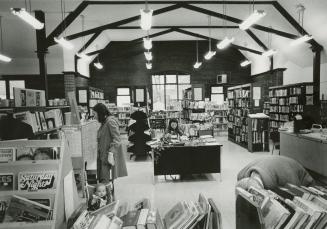Picture of library interior with beamed ceiling and crowded bookshelves and woman with a child …
