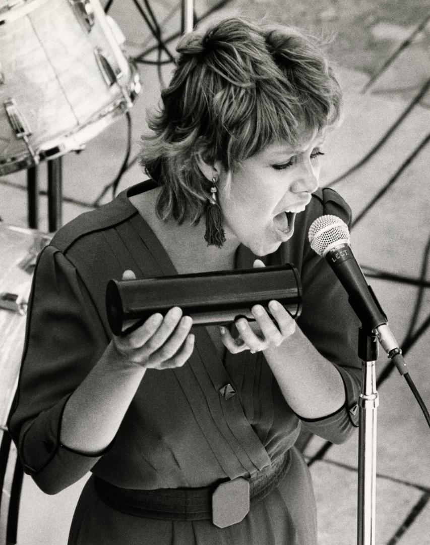 From above, a woman sings into a microphone holding a rhythm shaker. 