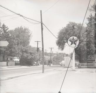Photograph of street with Texaco sign on rights and trees and telephone poles. 