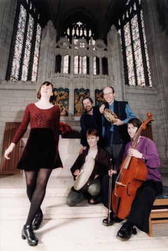 In church, stained glass windows behind step dancer. To her right, 4 musician, 3 men with Celti…