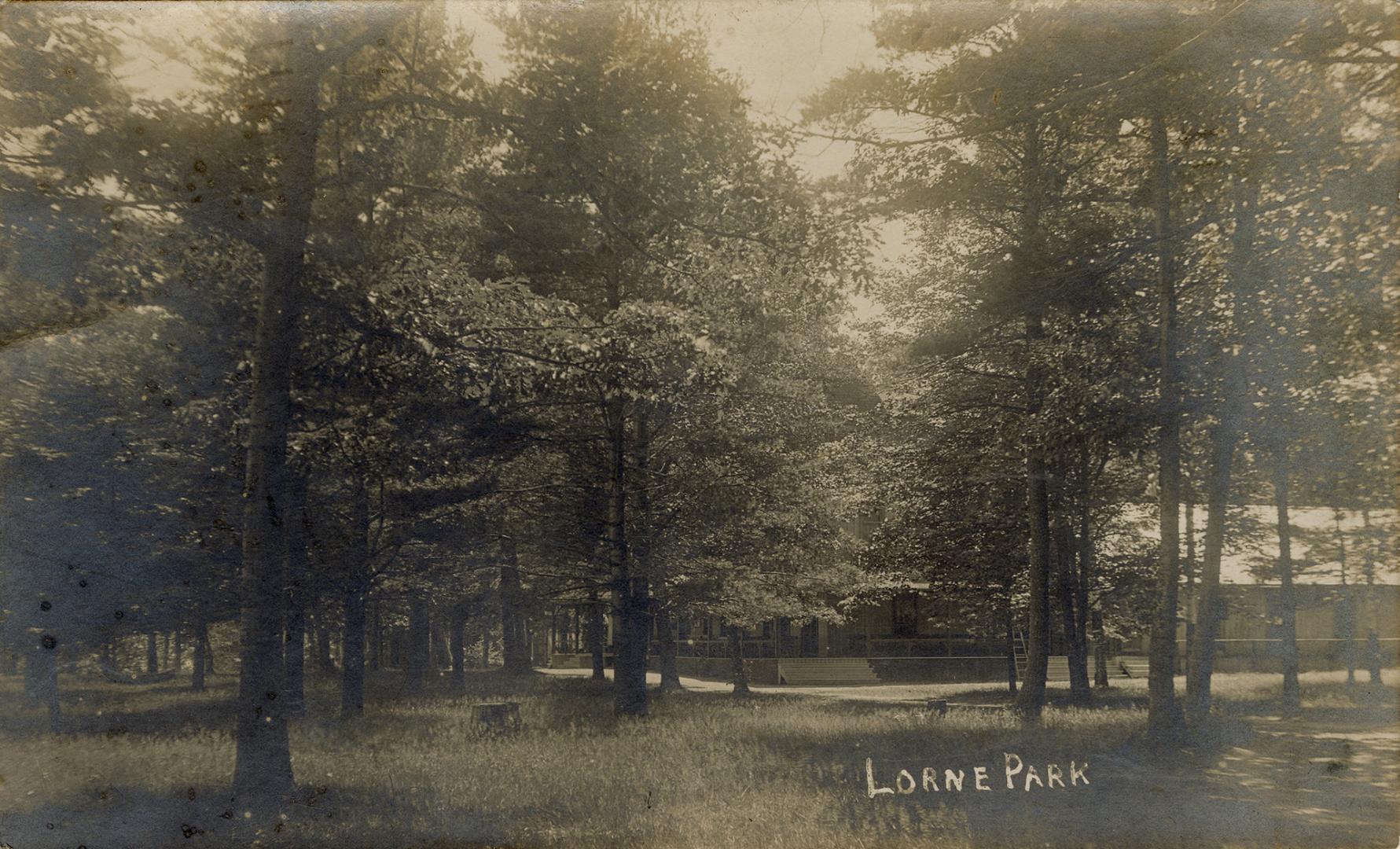 Black and white photograph of rustic buildings in a wooded area.