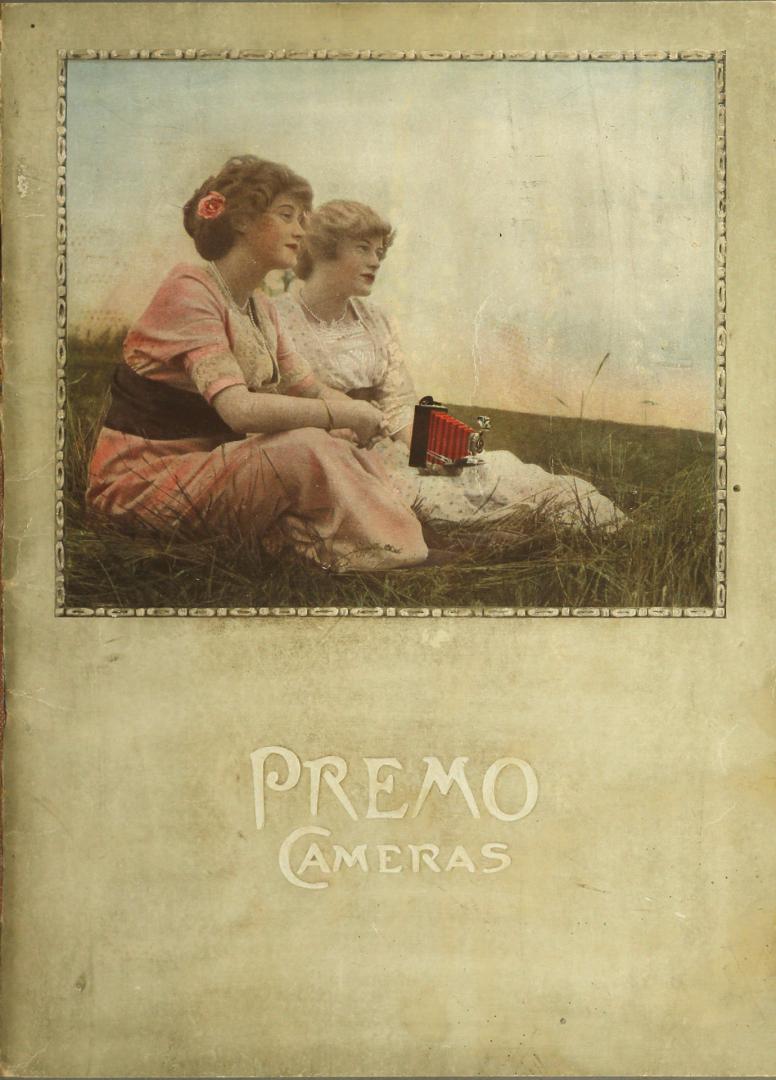 Coloured image of two women seated on the ground in a field with a camera